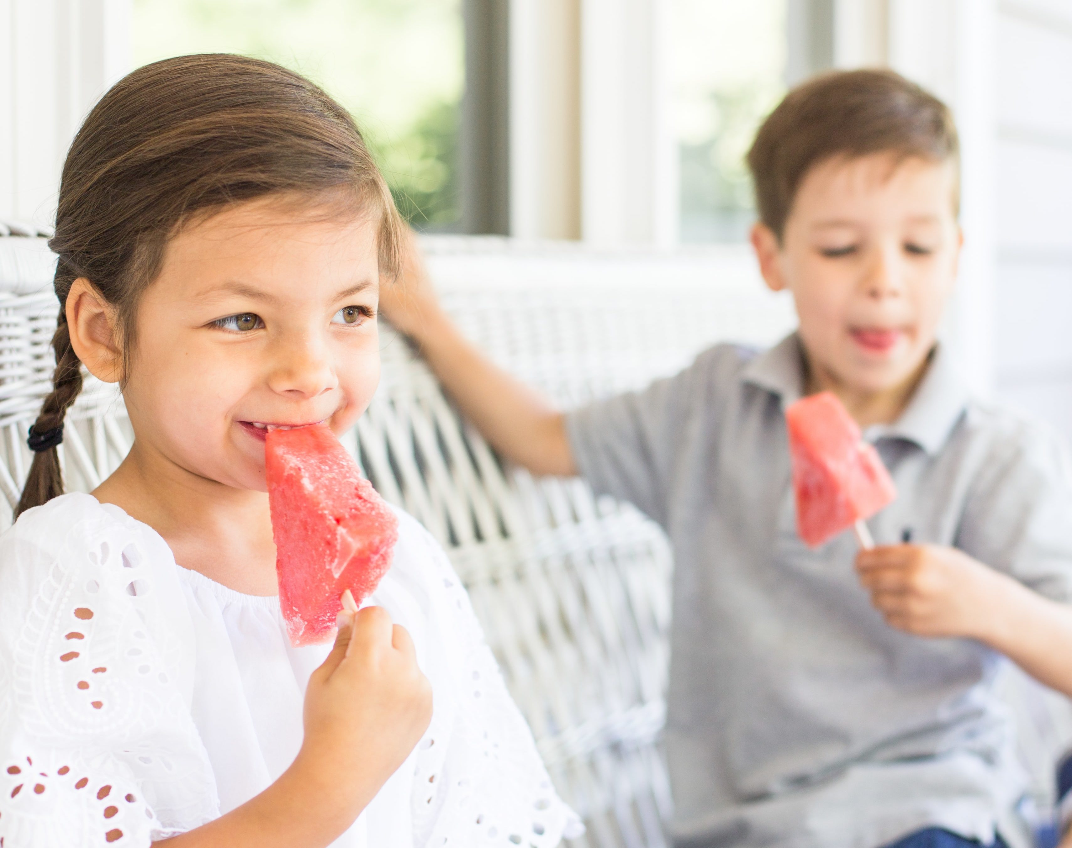 Two kids eat watermelon popsicles on their front porch